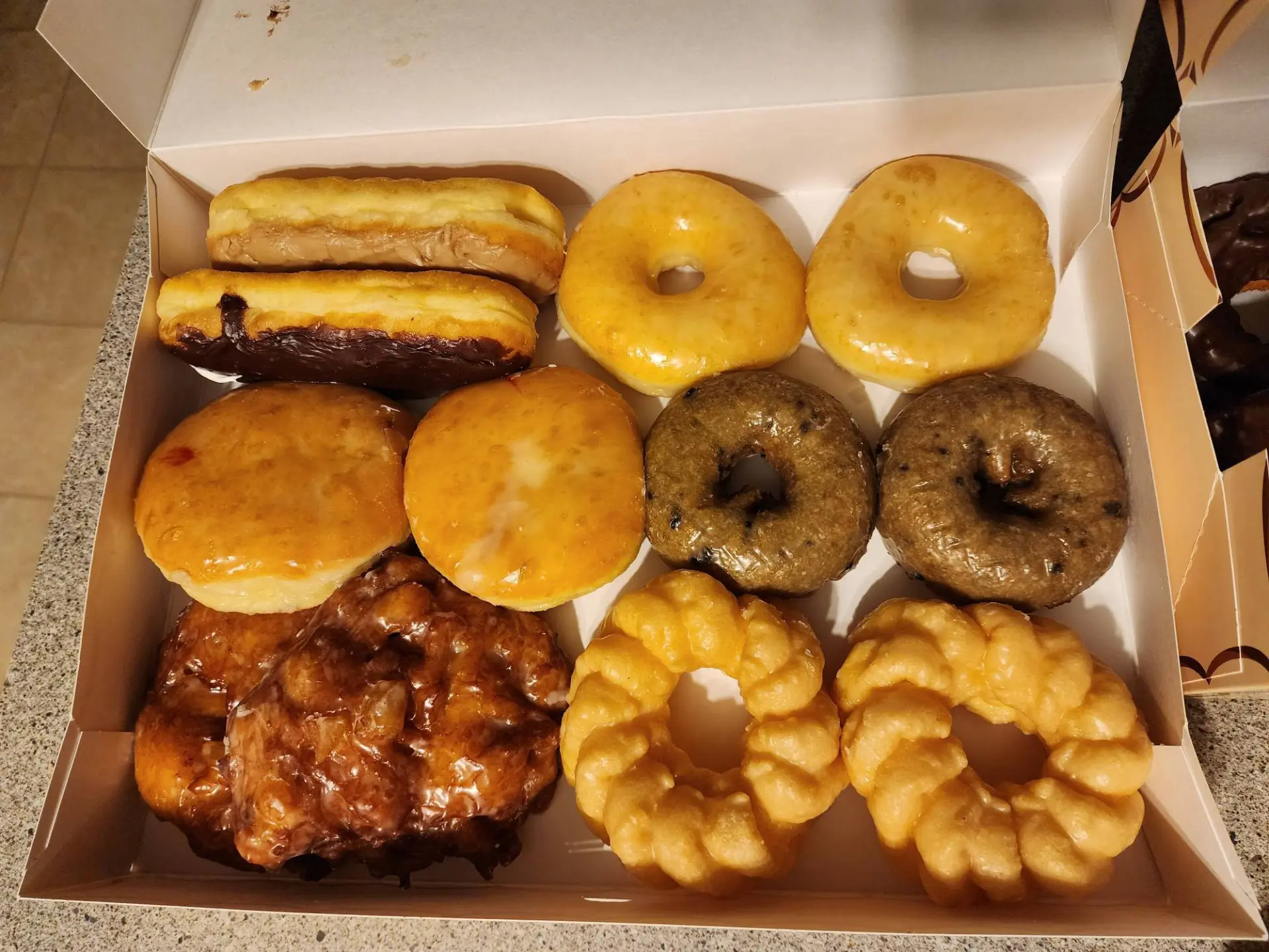 A box of long johns, glazed, jelly-filled, blueberry cake and French cruller-style donuts with an apple fritter